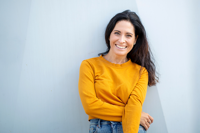 smiling woman in a yellow shirt and jeans on a blue wall